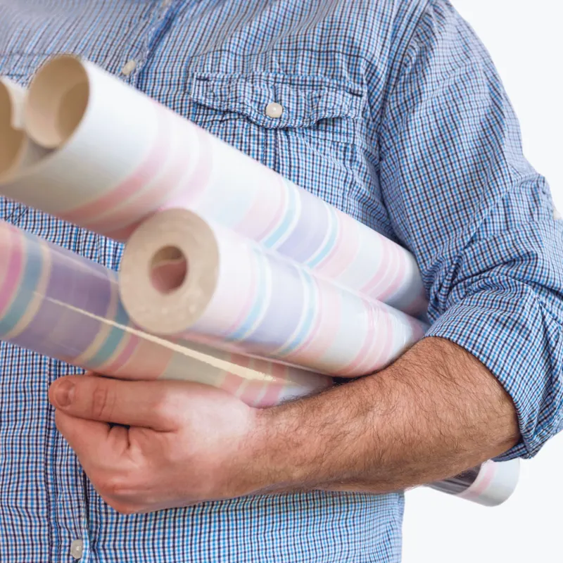 A man holding rolls of patterned wallpaper