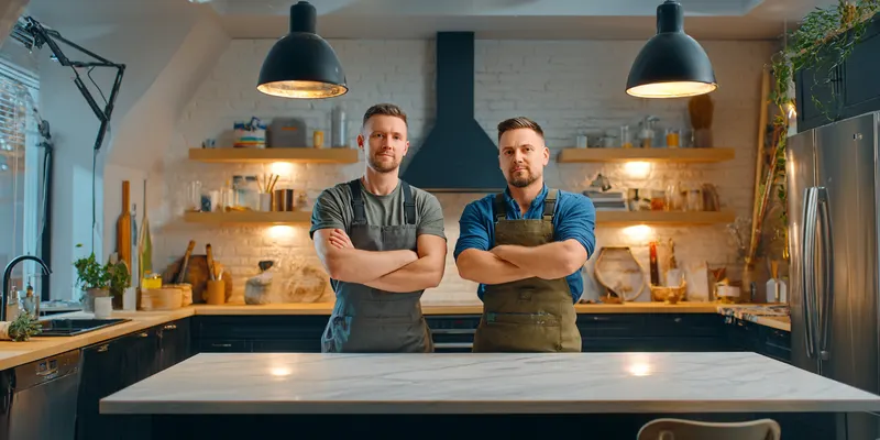 Two smiling men in work clothes with arms crossed in a kitchen
